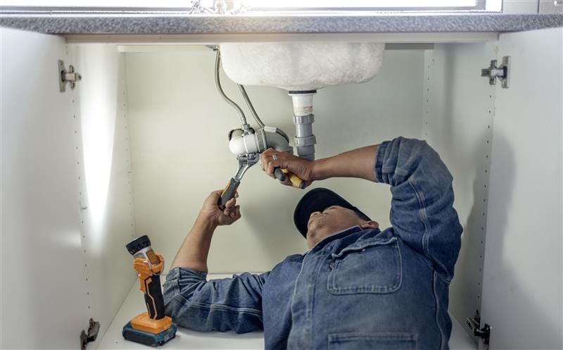 Plumber repairing pipes beneath a bathroom sink in Millbrae
